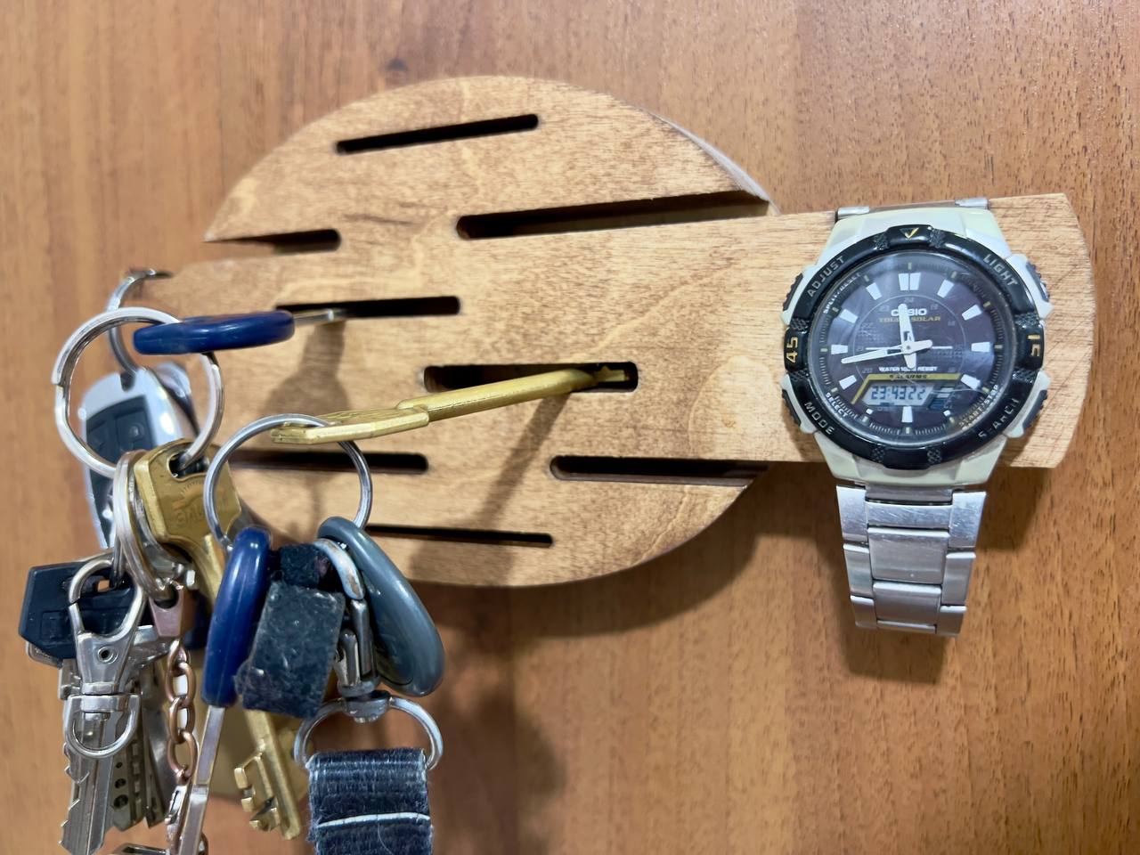The minimalist wooden key holder mounted on a white wall in an entryway, with keys hanging from it.